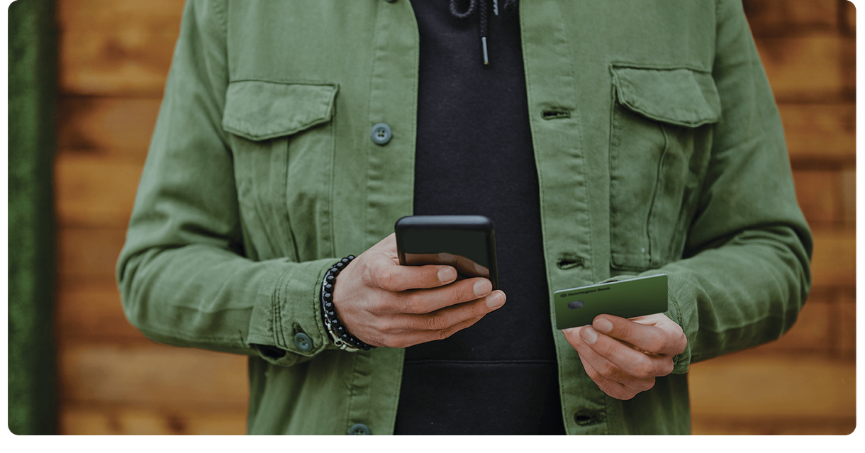 A customer holds a phone and a green debit card