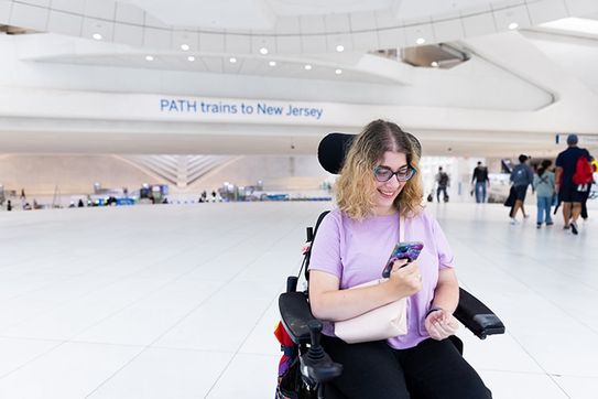 A rider in a power wheelchair uses a phone at a PATH station