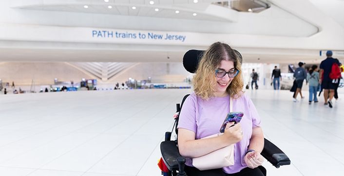 A rider in a power wheelchair uses a phone at a PATH station