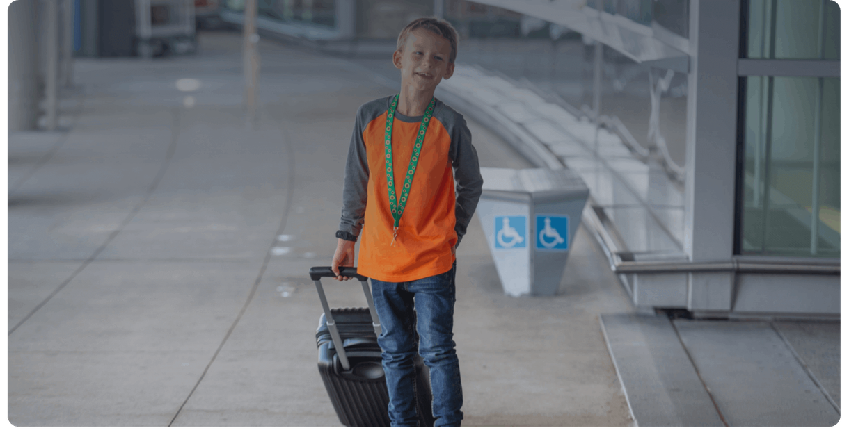A child wearing a sunflower lanyard walks through the airport with a suitcase