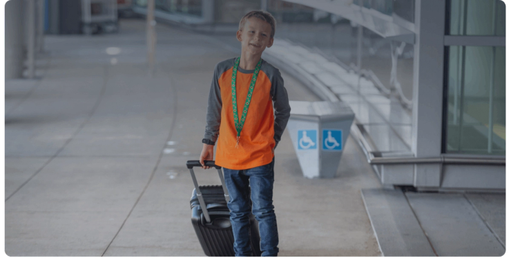 A child wearing a sunflower lanyard walks through the airport with a suitcase