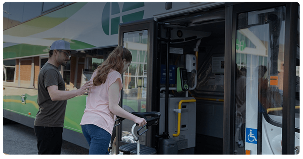A rider with a walker boards a GO bus with help from another passenger