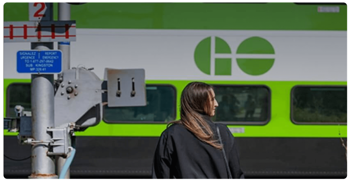 A pedestrian waits at a rail crossing as a GO train passes