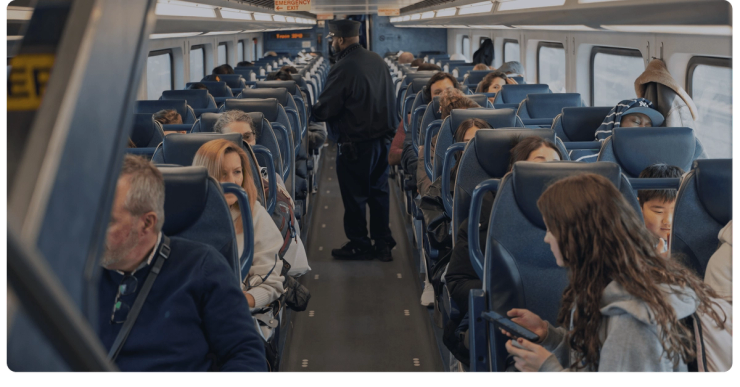 Riders in their seats as a conductor walks the aisle of an NJ TRANSIT train