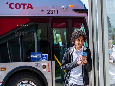 A rider looks at a phone while stepping off a COTA bus