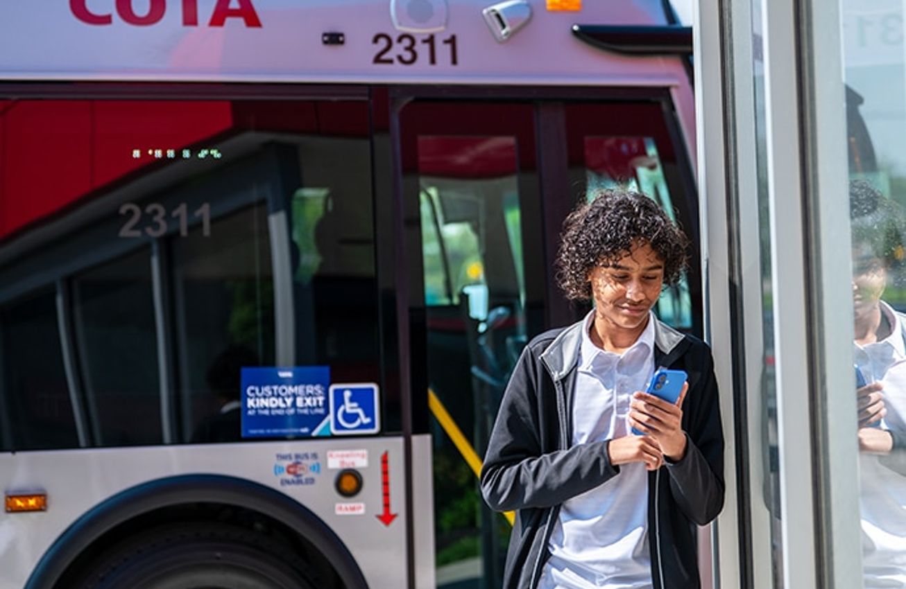 A rider looks at a phone while stepping off a COTA bus