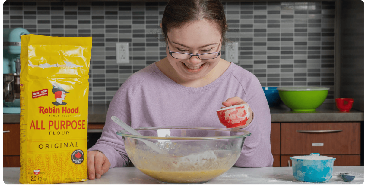 A baker mixes banana bread batter beside a bag of Robin Hood flour