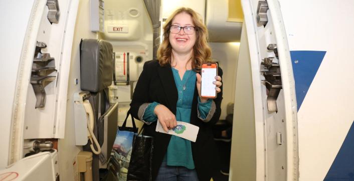 A traveller holding a phone smiles in the doorway of an airplane