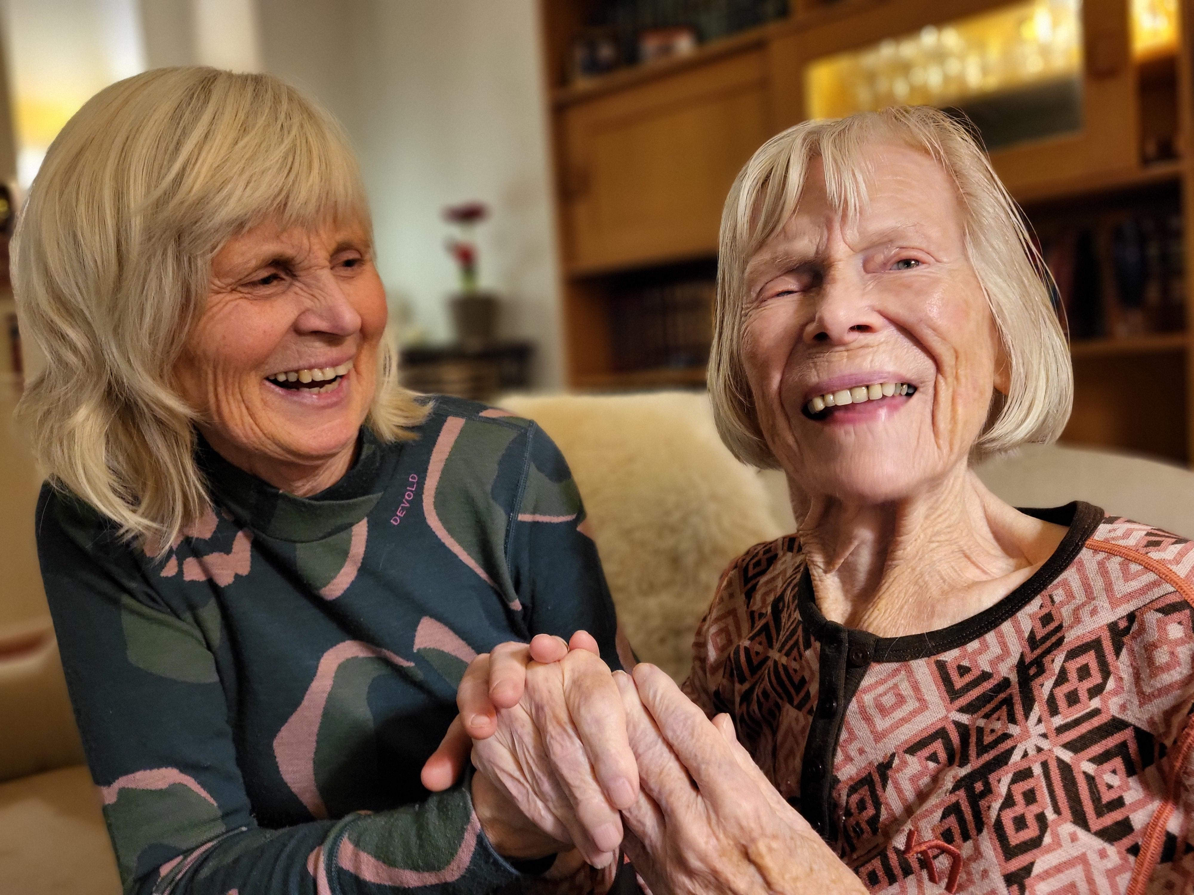 two elderly women are sitting on a couch holding hands and smiling .