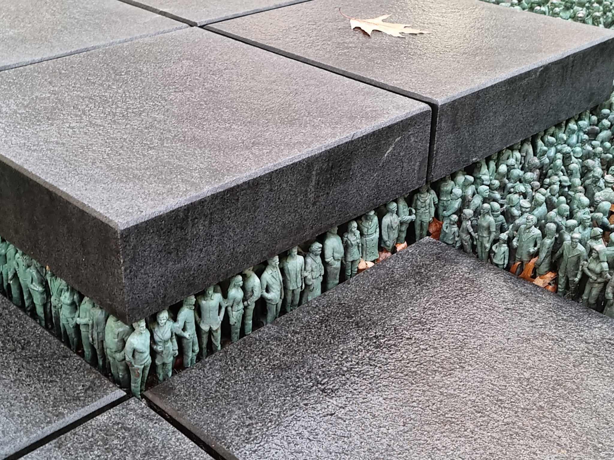 a statue of a group of people standing next to each other on a sidewalk .