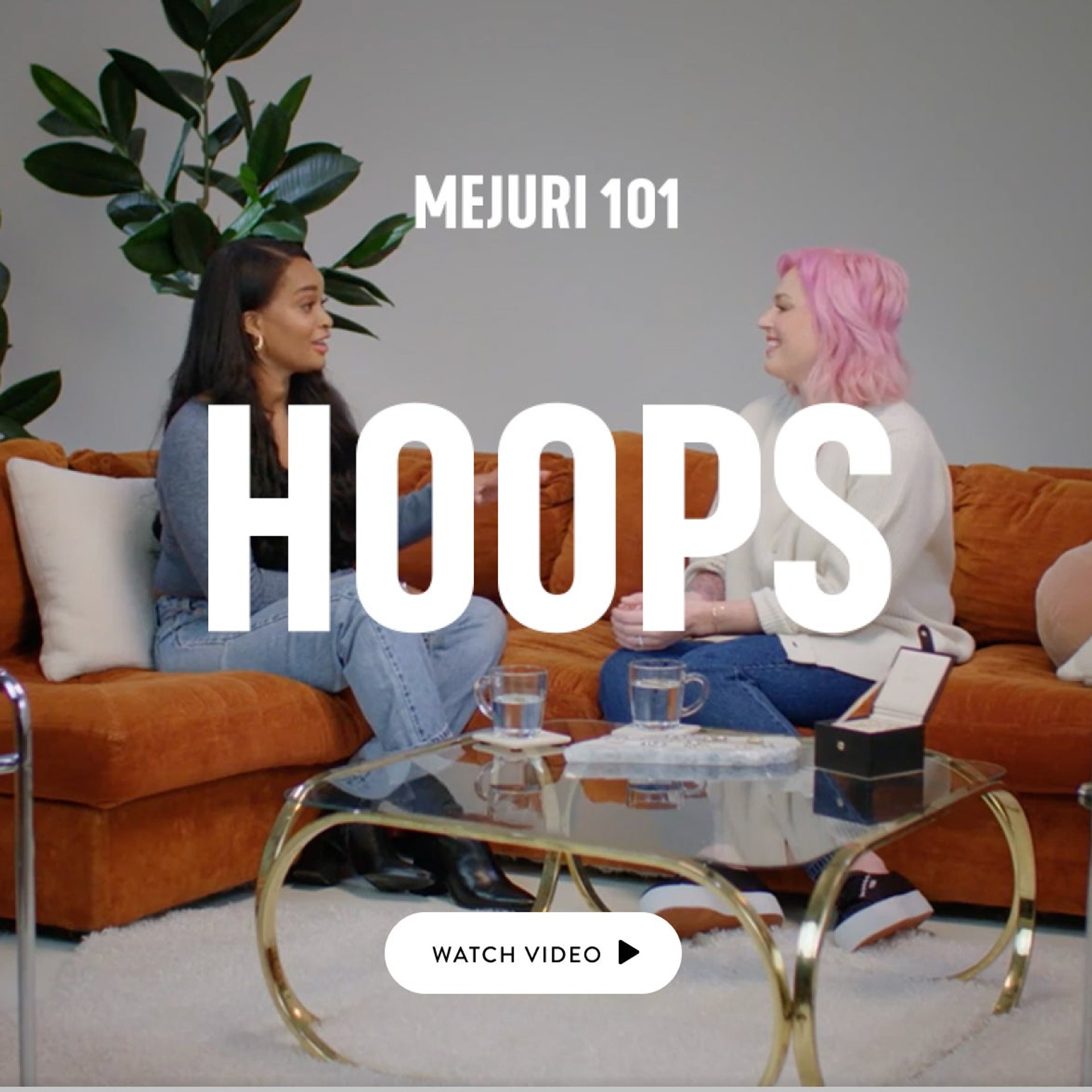 2 women sitting on rust colored couch. Title of video written over top reads: Mejuri 101 Hoops with a button to watch video