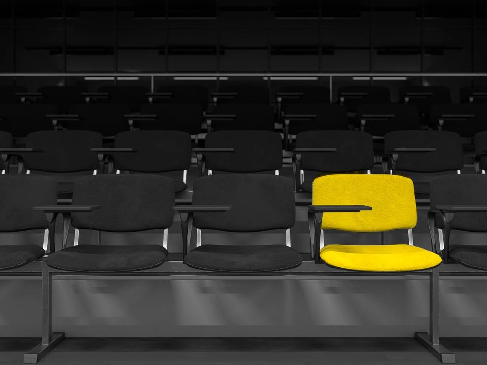 A single yellow seat standing out in rows of dark lecture-theatre seating