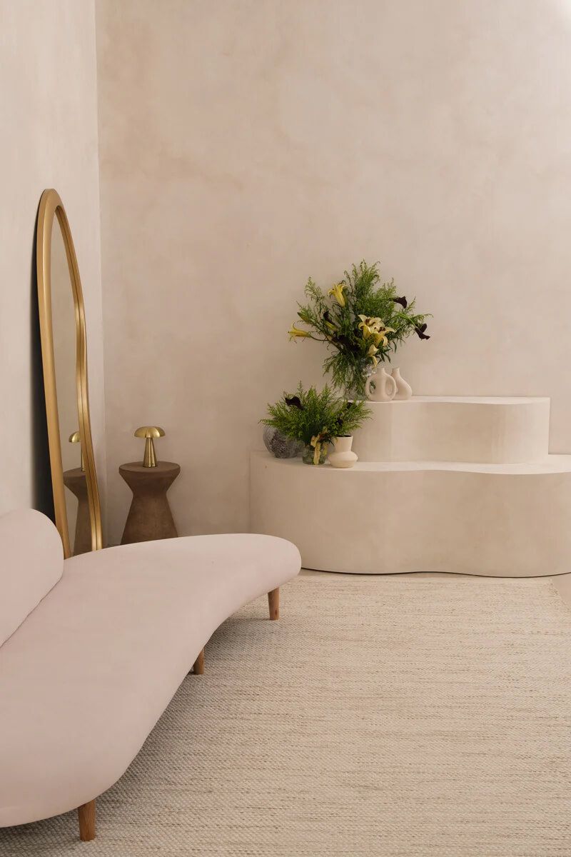 Sophisticated and serene interior with a plush curved sofa, large round mirror reflecting soft natural light, and lush green plants, embodying the Feng Shui principles of flow and tranquility in home design
