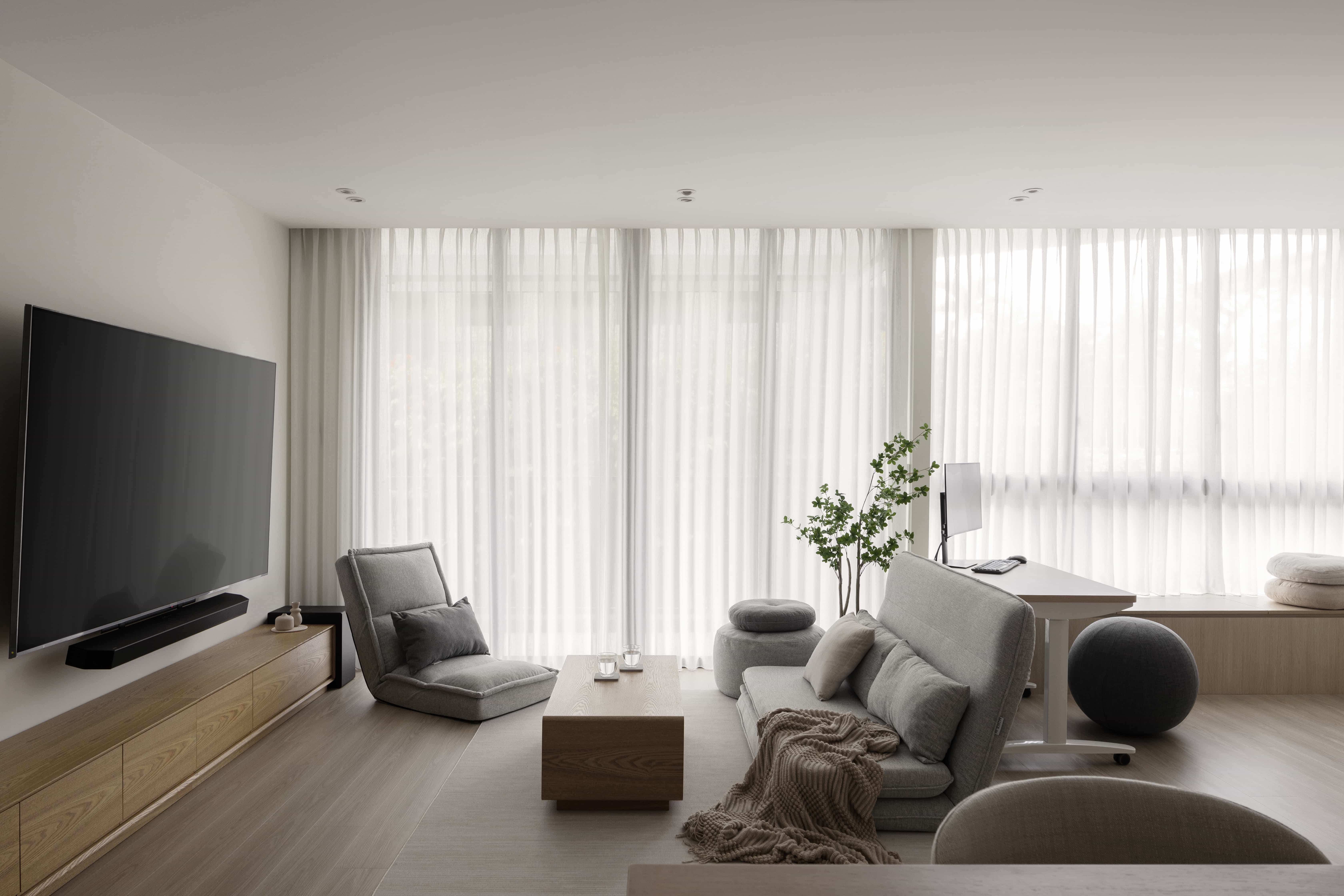Scandinavian living room designed by 6AM Spaces with large TV, grey sofa, and floor-to-ceiling sheer curtains.