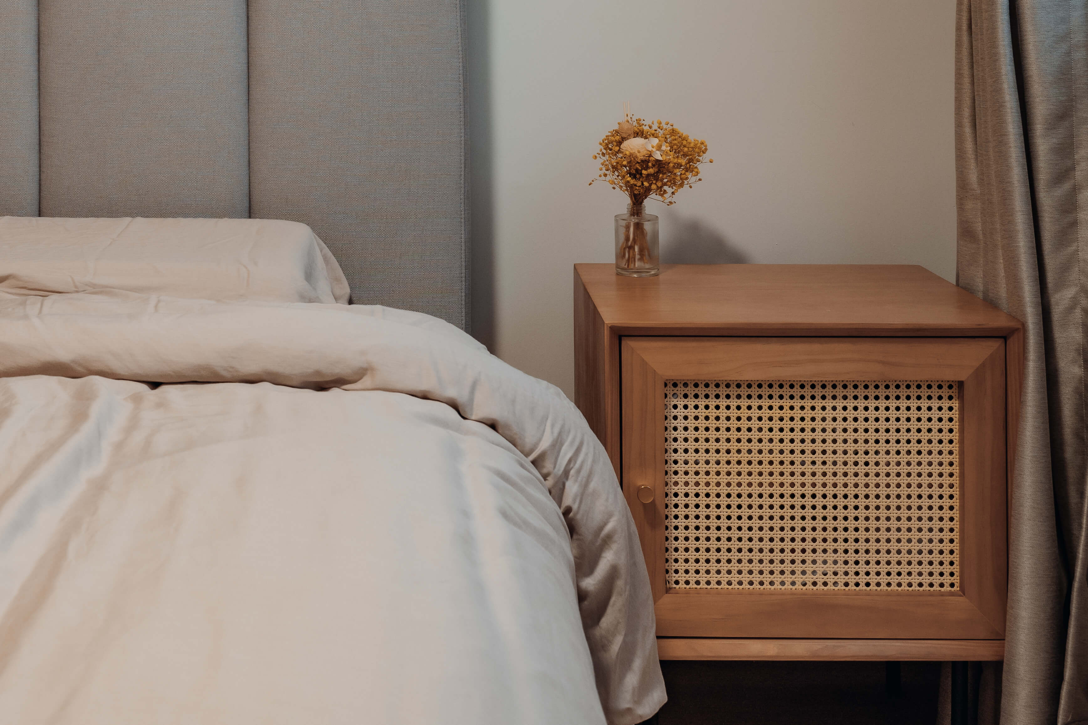 Serene Scandinavian bedroom design with light bedding, a wooden bedside table, and a small vase of dried flowers.