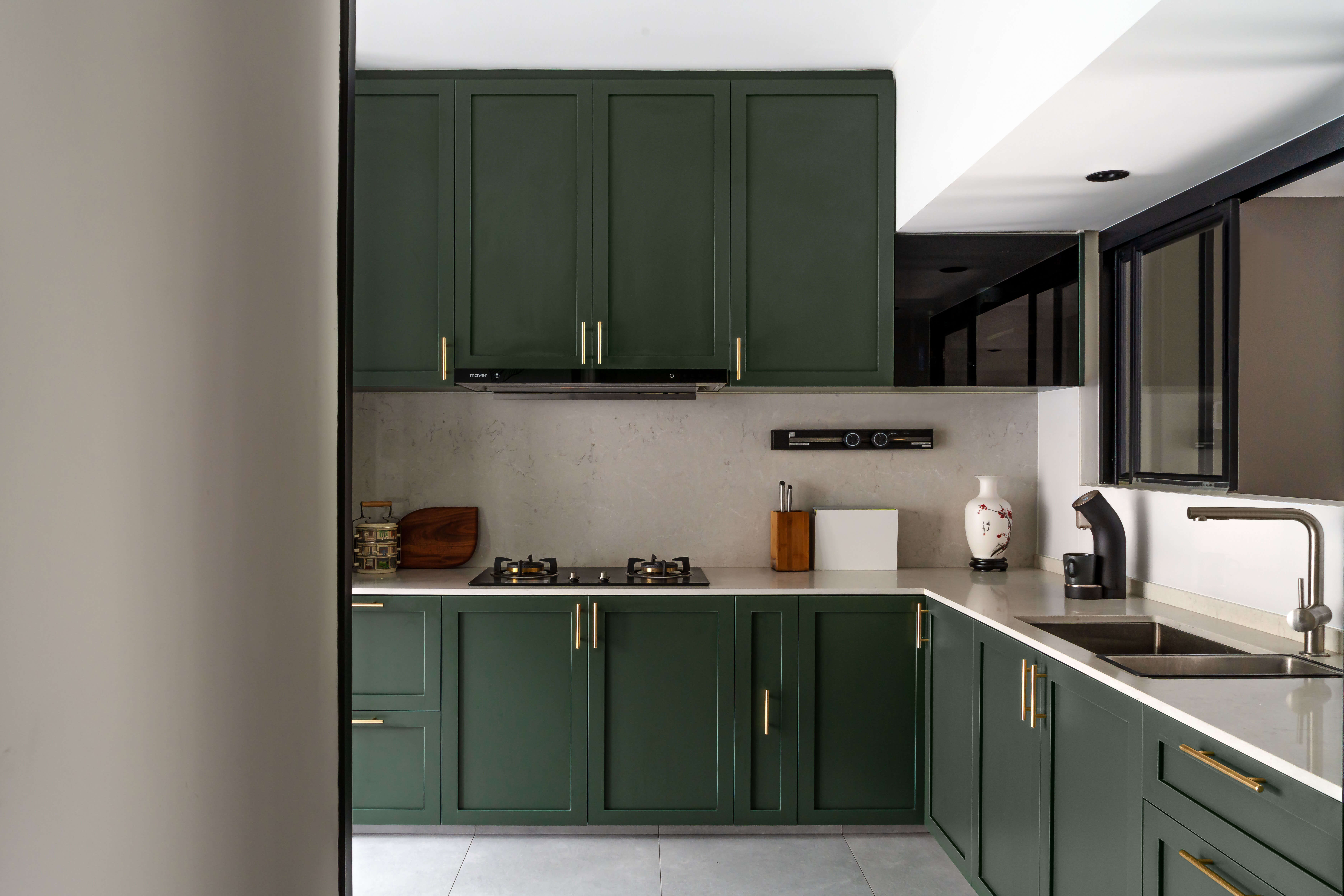 Sophisticated kitchen with dark green cabinets, brass hardware, and marble backsplash, featuring modern appliances and sleek design elements.