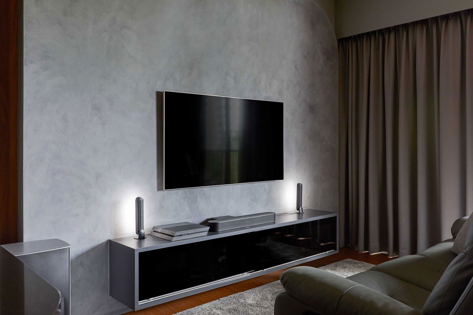 Sleek and contemporary TV wall design with mounted flat-screen TV, ambient lighting, and modern dark-toned console in a room with textured gray walls and elegant drapery.