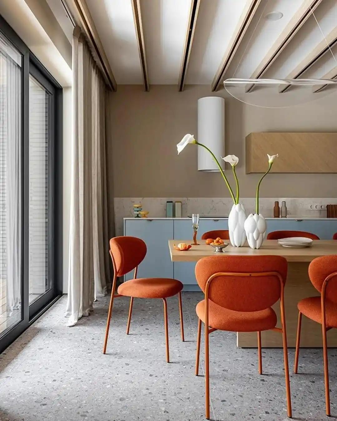 Modern dining room with burnt-orange upholstered chairs, pale-blue cabinets, terrazzo floor and a light-wood table.