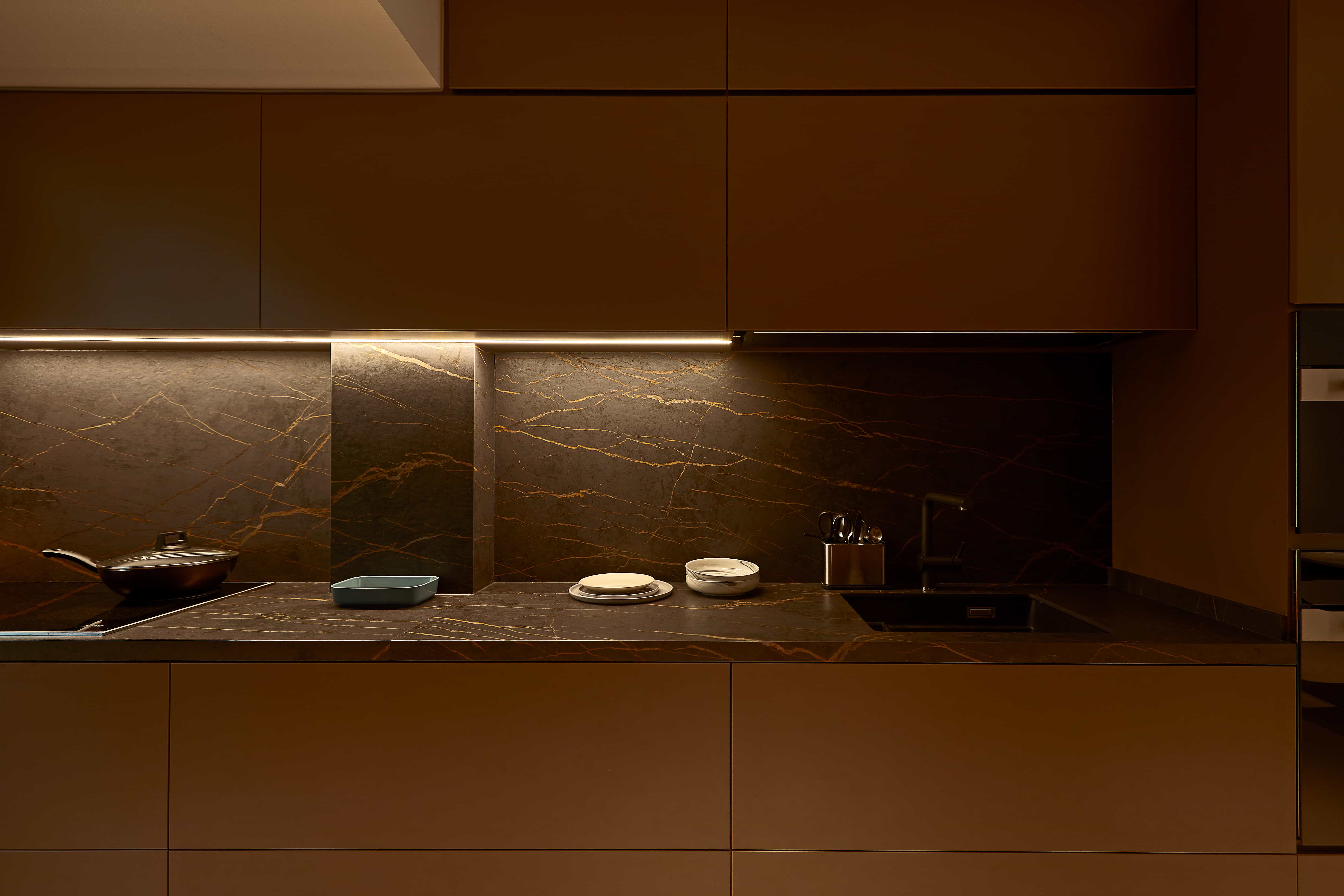 Elegant kitchen with dark cabinetry, integrated lighting, and a modern aesthetic, designed by 6AM Spaces.