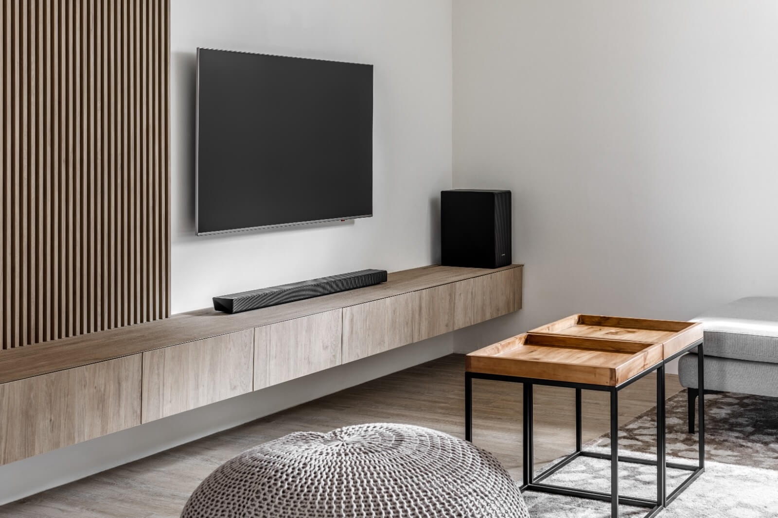 Minimalist Scandinavian living room with a wooden accent wall, floating TV console, and black modern lighting fixtures.