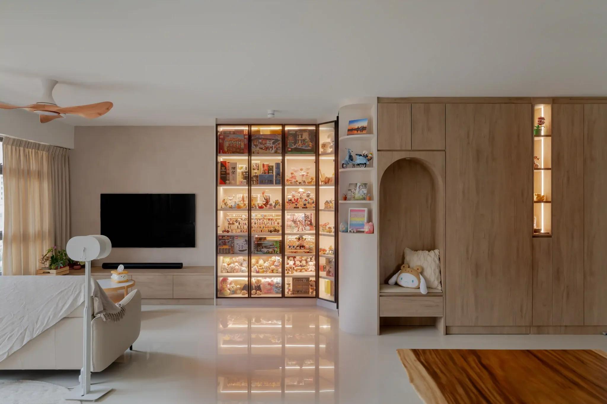 Living room with illuminated glass display cabinet for collectibles, TV console, and a curved niche bench in light wood.