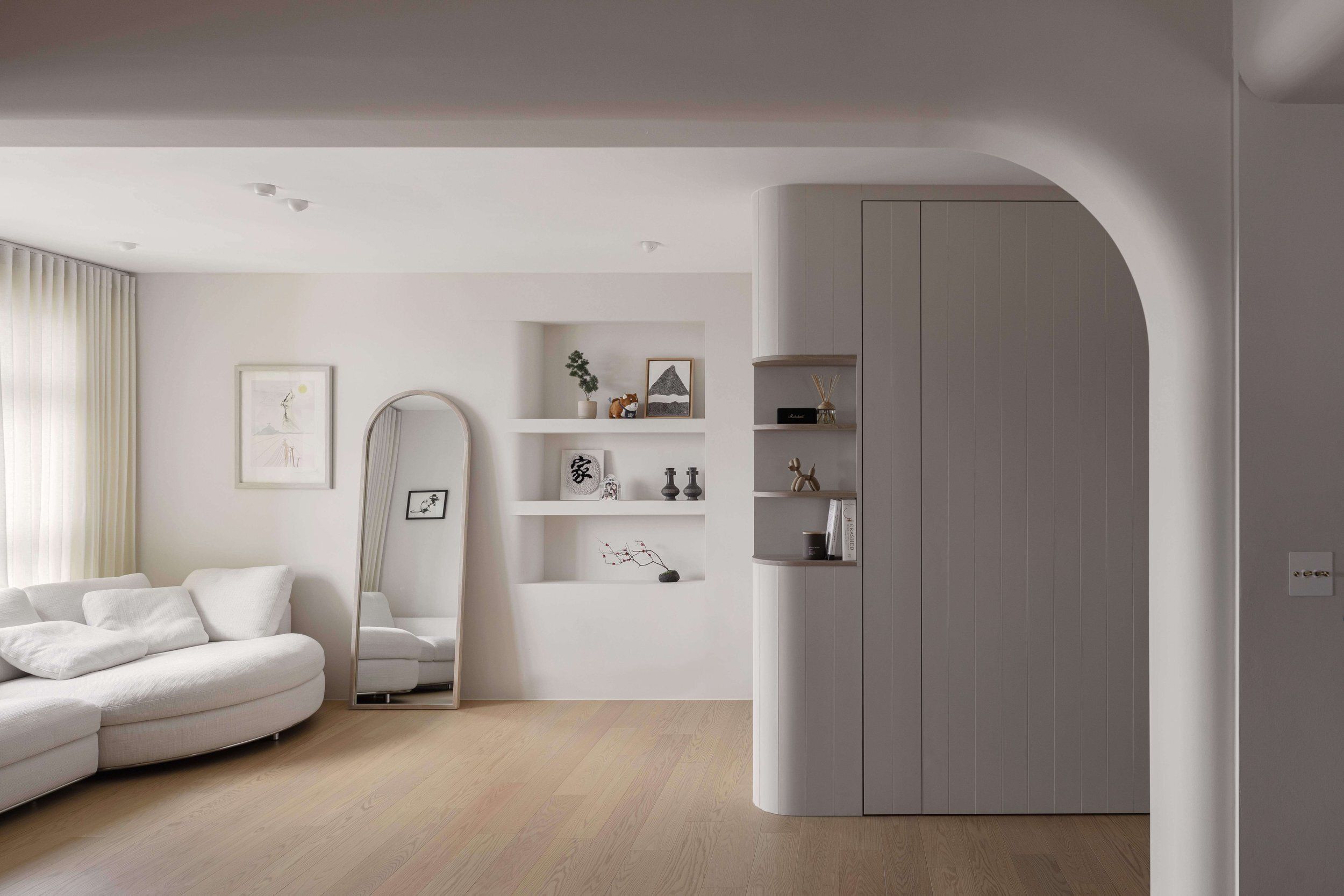 Minimalist living space featuring a gently curved archway, built-in shelving, and soft edges.