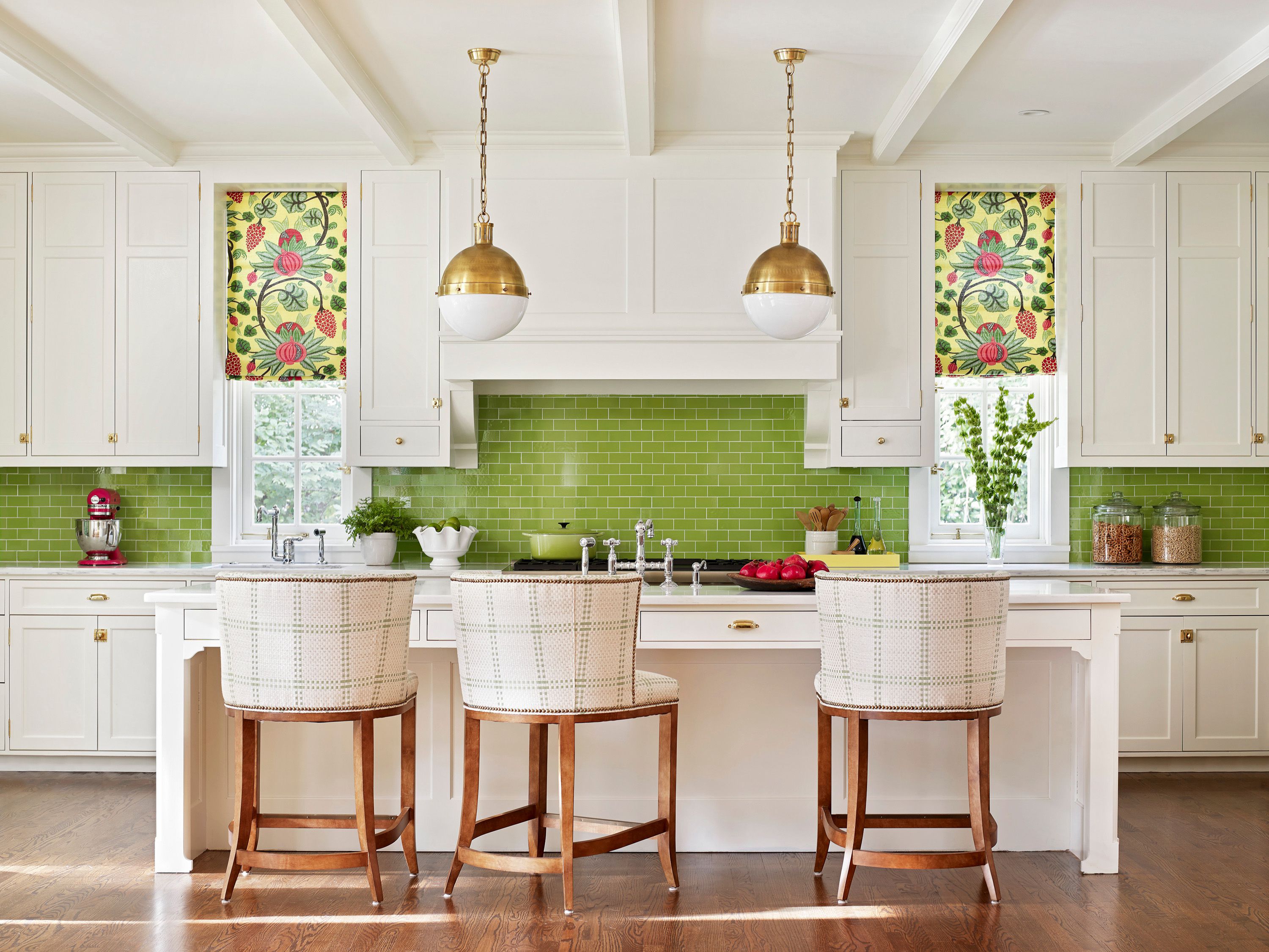 A kitchen with a green tile backsplash, gold pendant lights, and white furniture, creating a vibrant cooking space.