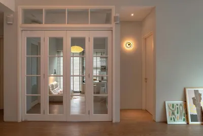 Bifold white framed glass french doors segregating the study room from the living area of warm grey walls and wooden flooring