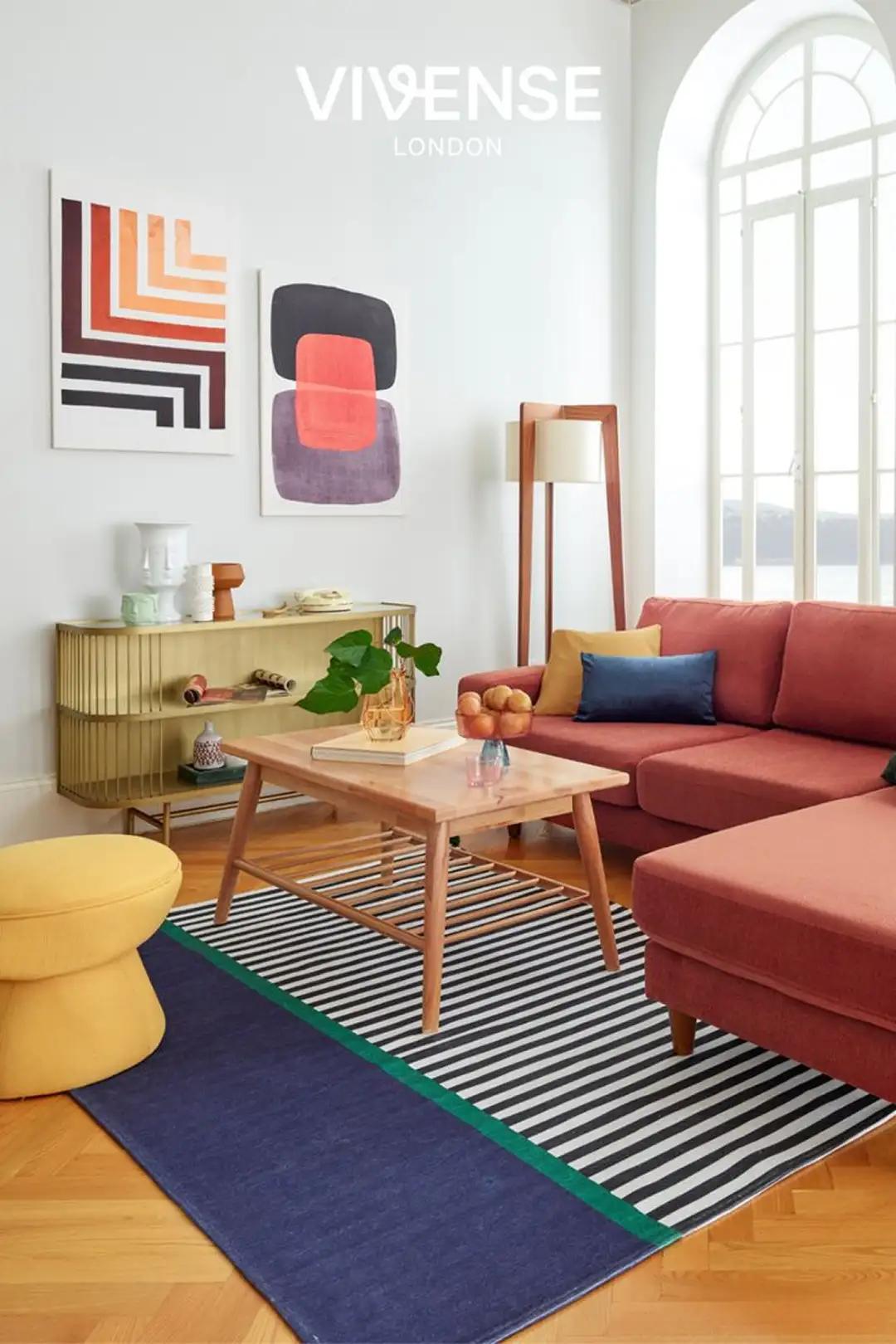 Playful living room with coral sectional, mustard stool, striped rug and graphic wall art in a bright, sunlit space.