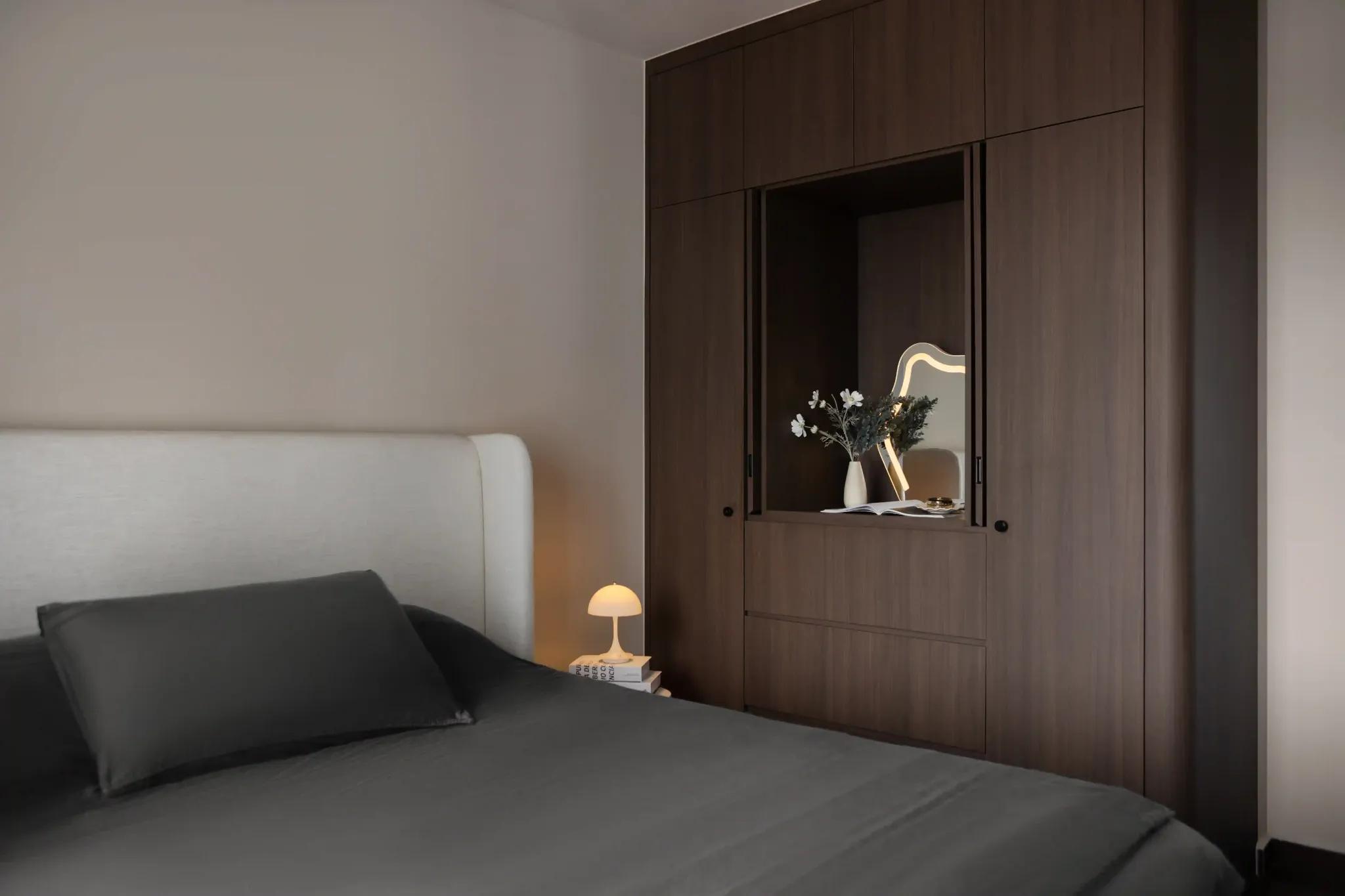 Built-in wardrobe in dark wood with sliding doors and a recessed vanity niche; upholstered headboard and mushroom lamp.