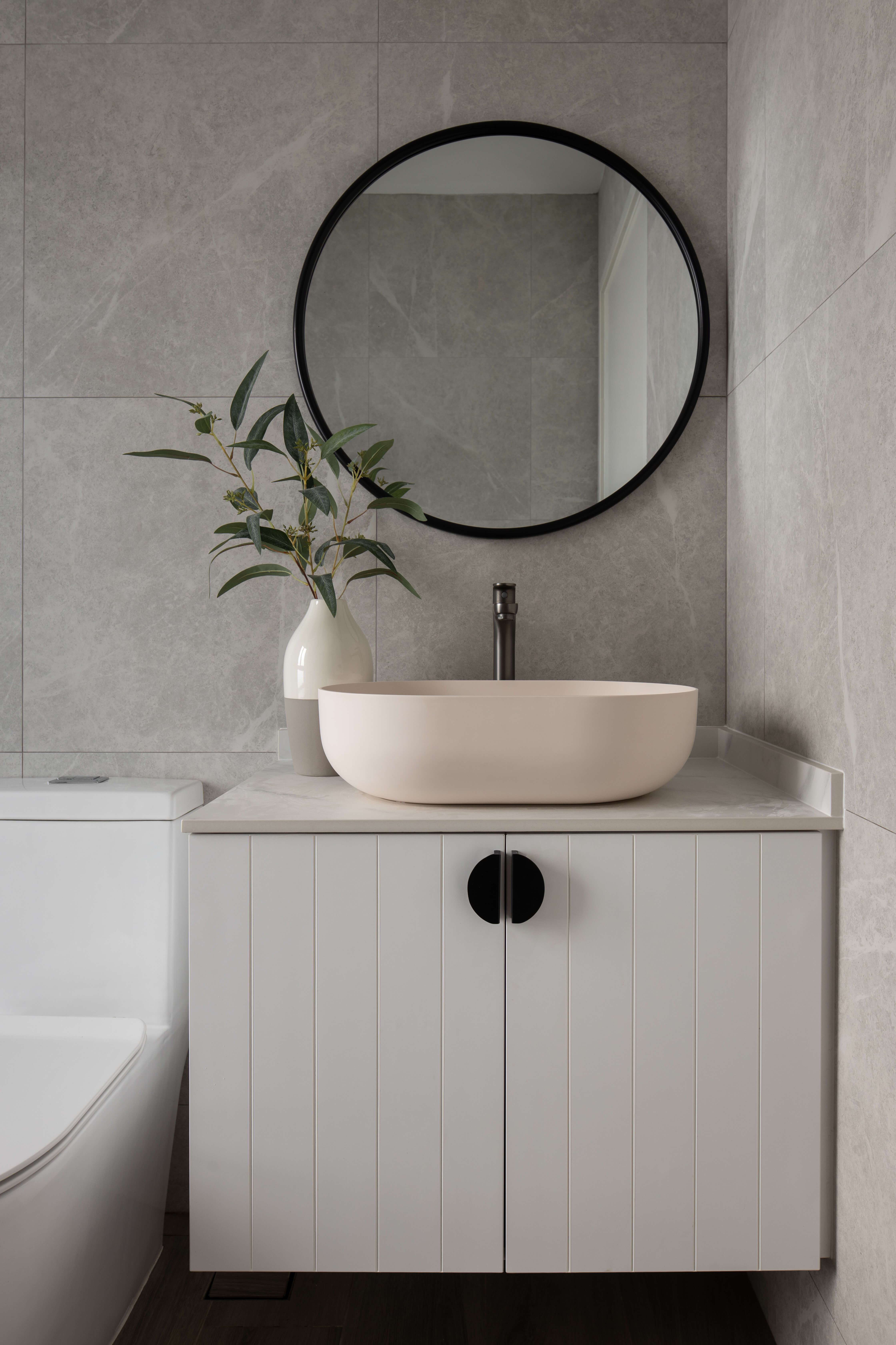 Minimalist bathroom with a round mirror above a modern sink and a white vanity unit.