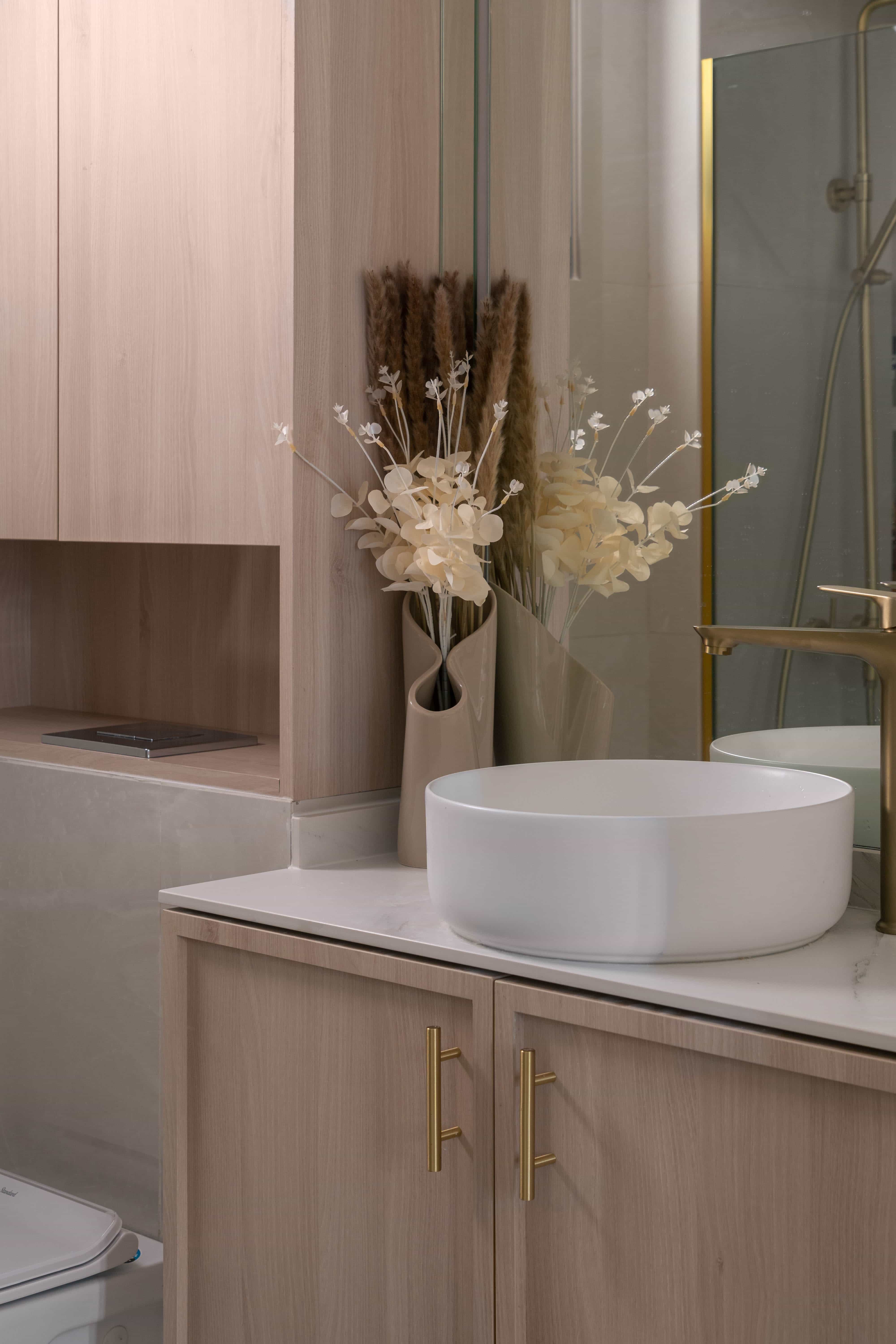 Elegant bathroom vanity with a white basin and gold accents, complemented by decorative dried flowers.