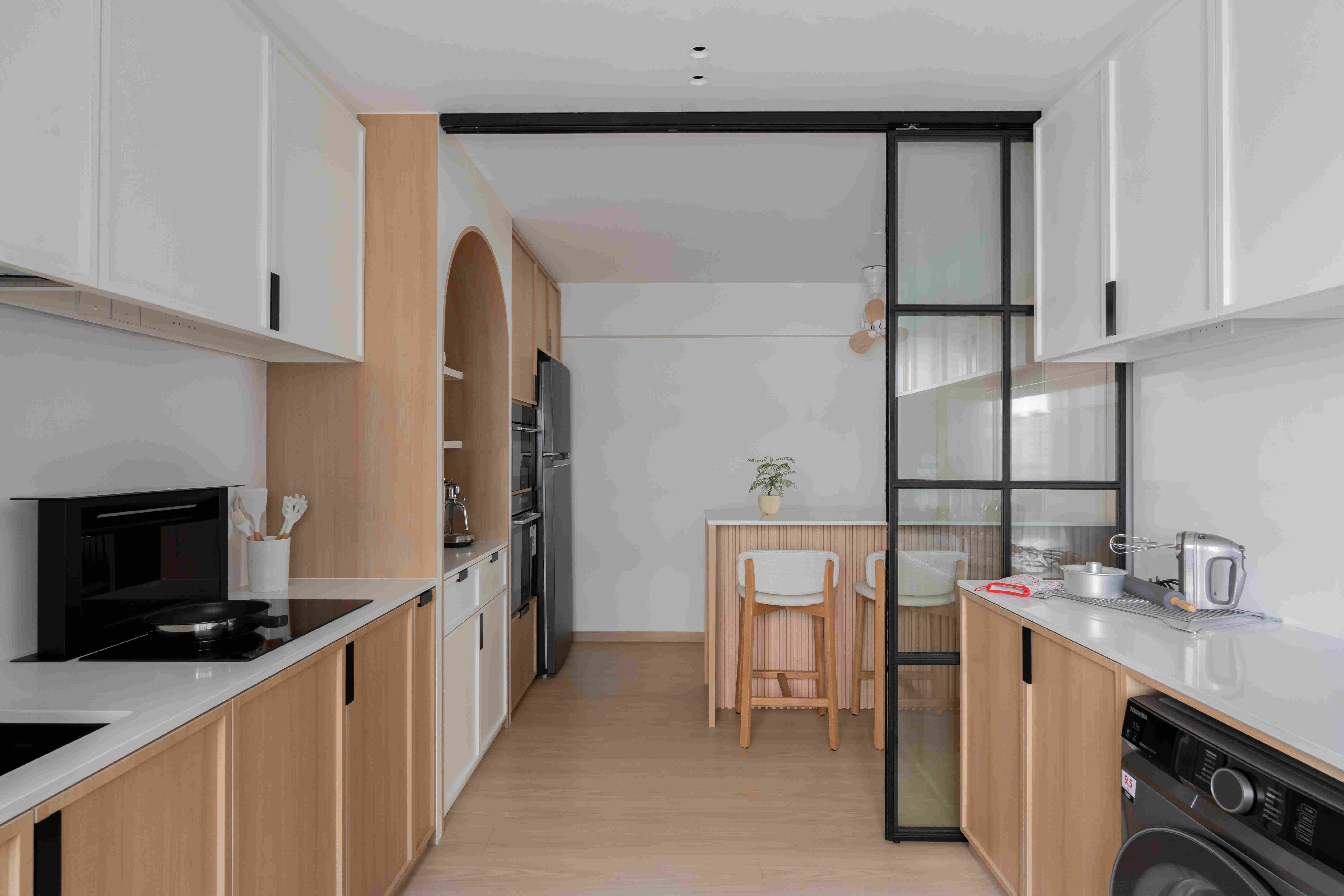 Streamlined galley kitchen featuring white and blonde cabinetry, arch display niche, and sliding glass screen that defines zones without walls.