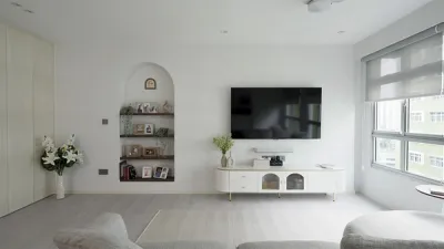 Frontal shot of the living room with a wall mounted television on white walls contrasted by soft grey flooring, window blinds and sofa