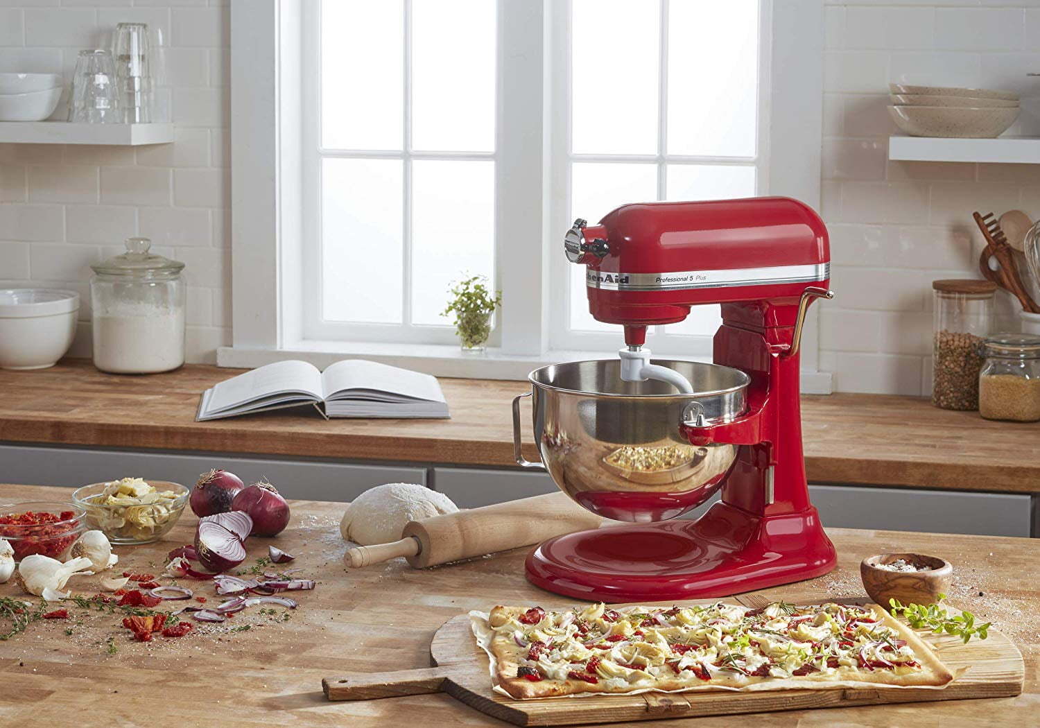 Iconic red stand mixer on a wooden countertop with dough and pizza ingredients.