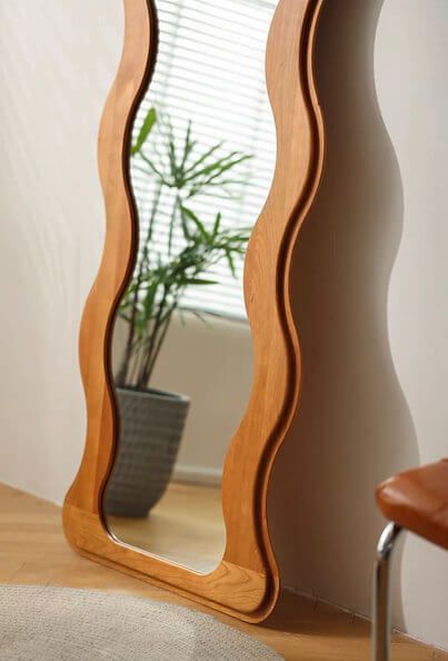 Unique wavy wooden mirror reflecting a peaceful corner with a green plant, embodying a blend of natural wood elements and the reflective qualities of Water in Feng Shui-inspired interior design