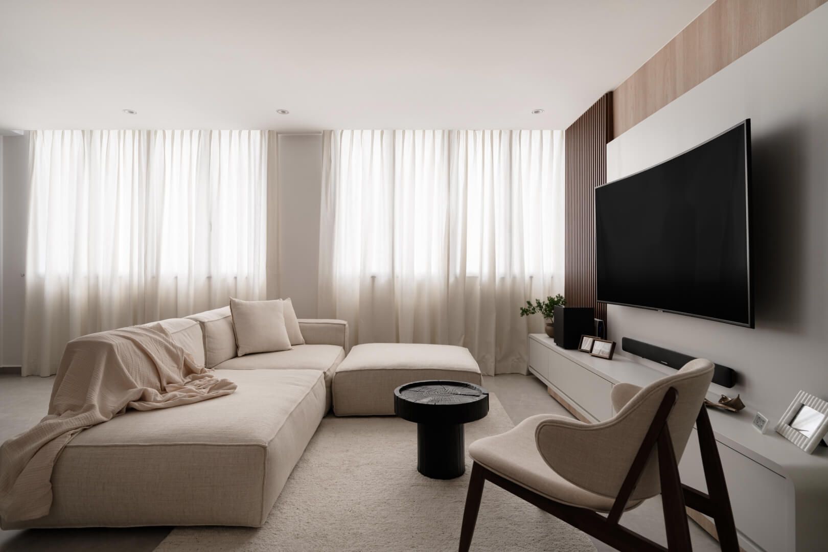 Elegant modern living room with a neutral color palette, featuring a plush sectional sofa, sheer curtains, and a minimalist entertainment unit.