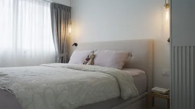 Plush beige bed frame within the bedroom beside grey drapes and white sheer curtains