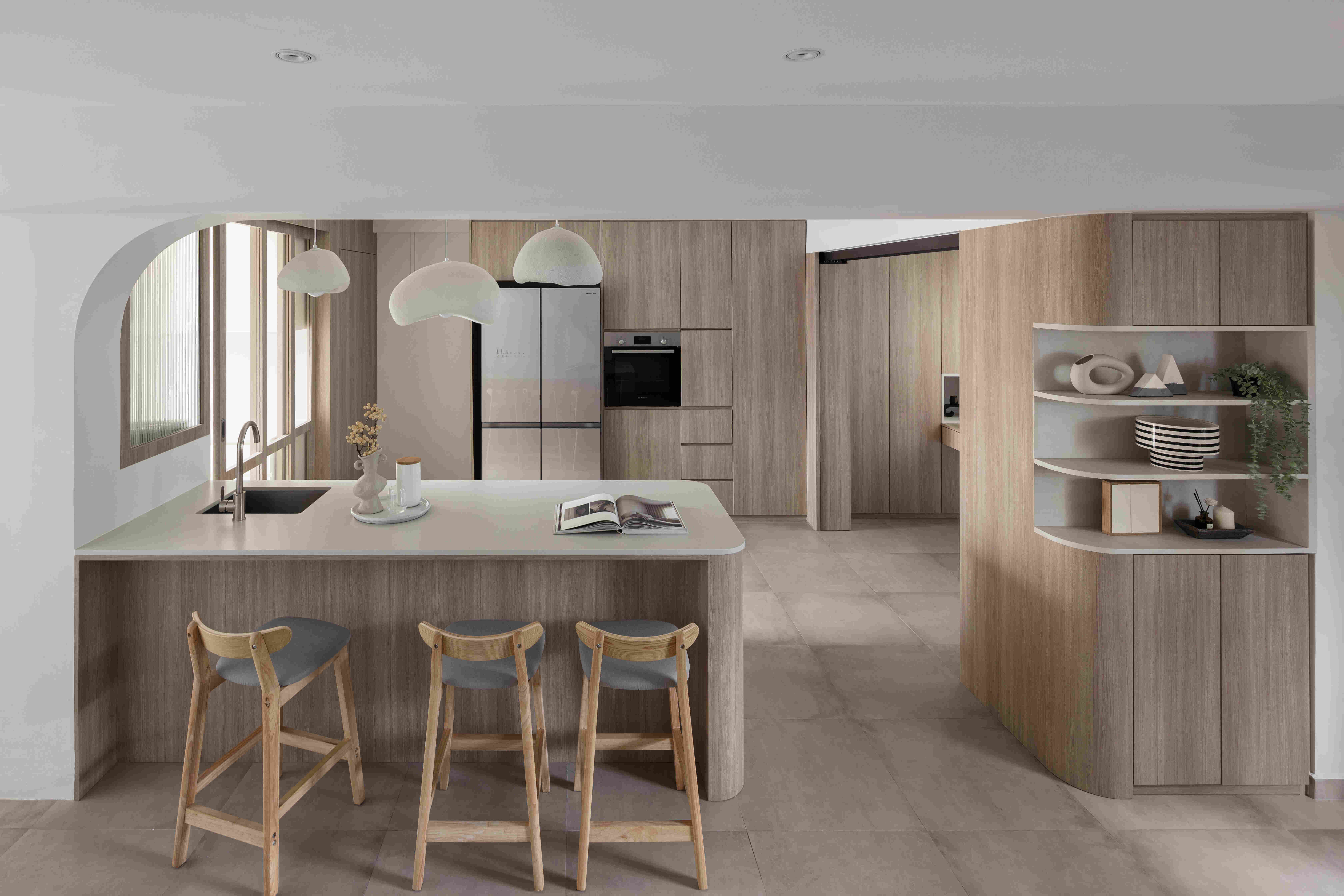 Light-oak kitchen with curved peninsula, minimalist pendant lamps, and integrated appliances creating a family-friendly workspace.