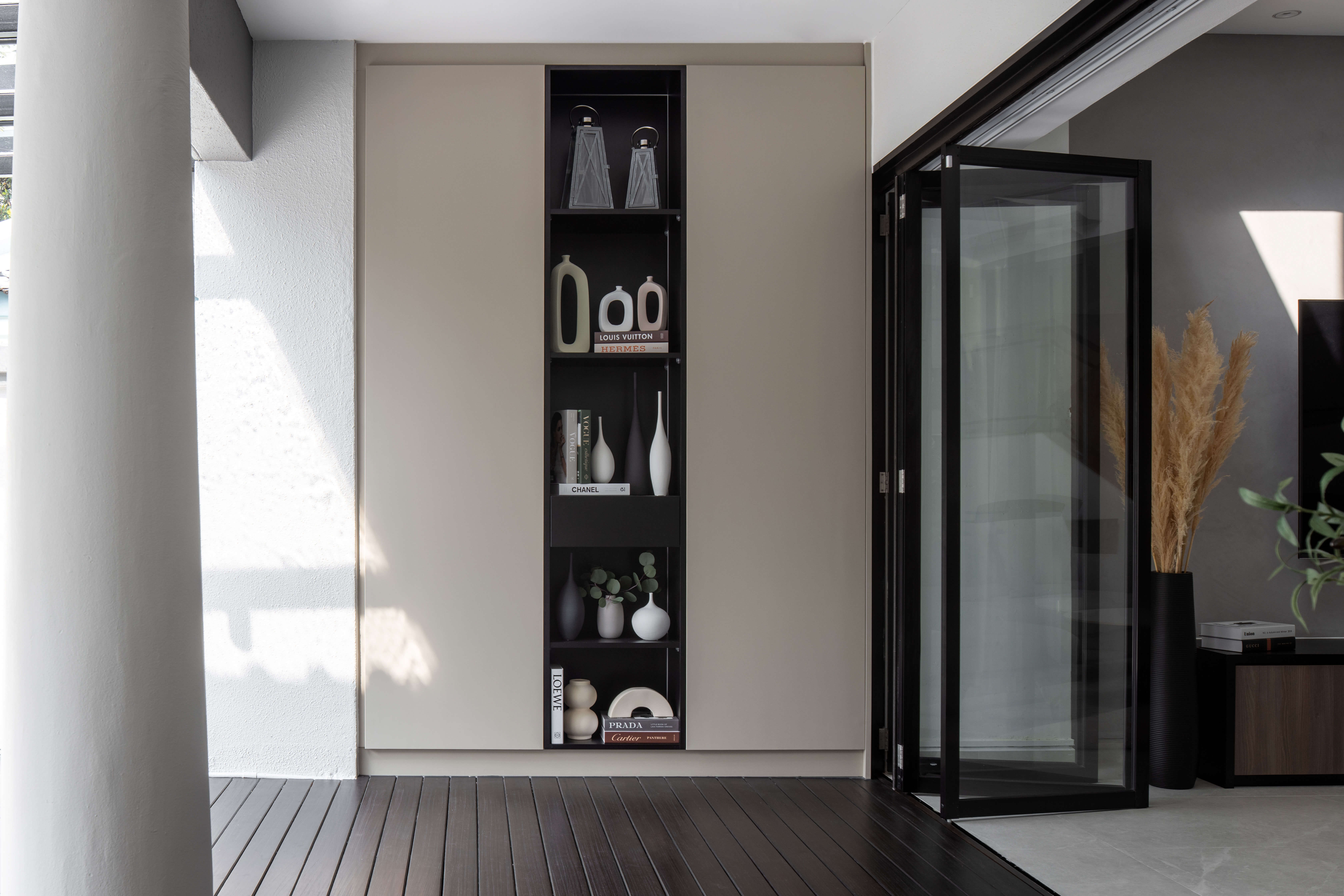 Chic display shelf with minimalist decor and designer books, nestled in a corner by glass-panelled doors, complementing the dark wooden flooring.