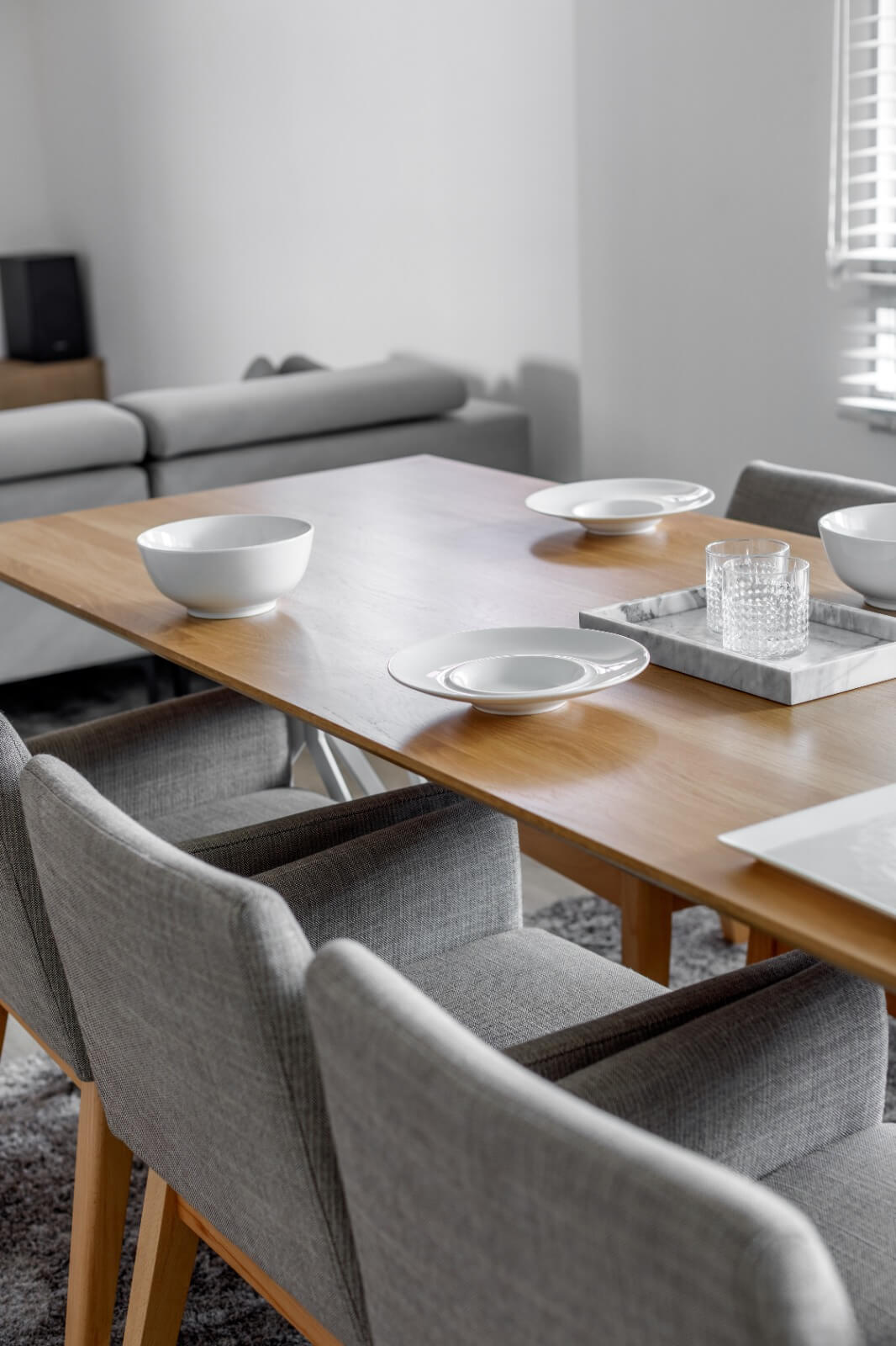 Minimalist dining room setup with a wooden table, gray chairs, and simple white dinnerware.