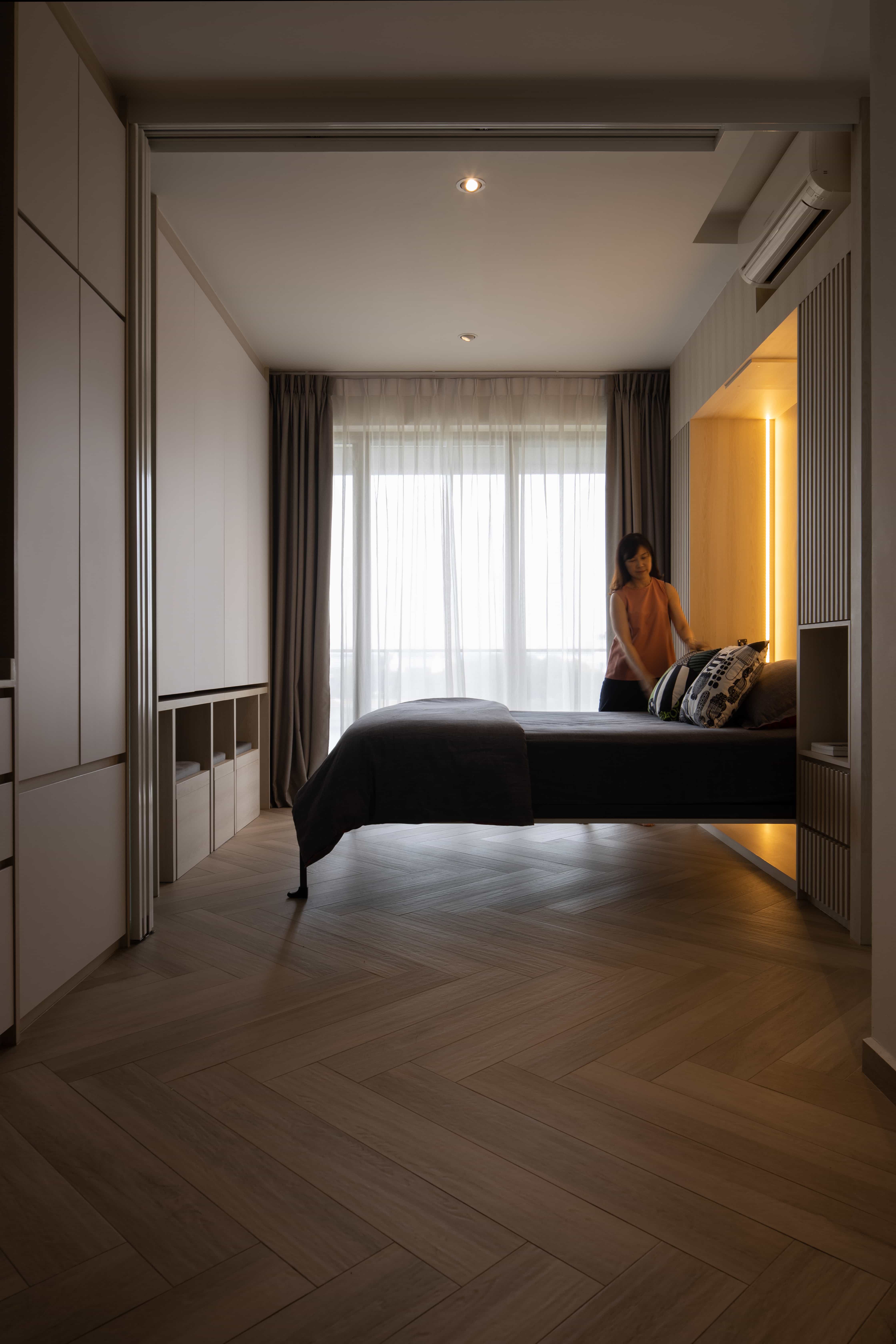 Stylish small bedroom with a back-lit Murphy bed being arranged.