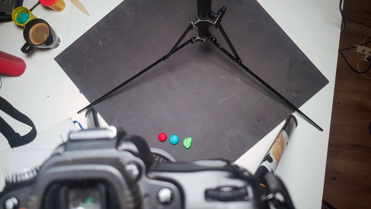 Perspektive von oben mit einer Kamera, die mit einem Stativ auf die schwarze Platte und die bunten Knetkugeln gerichtet ist.