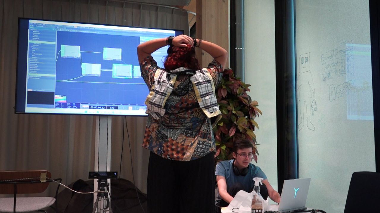 Aufnahme während des Demodays. Im Vordergrund steht eine Nutzerin, welche zum TV im Hintergrund gerichtet ist und die Arme hebt. Daneben steht Max und kontrolliert am Laptop den Prototypen.