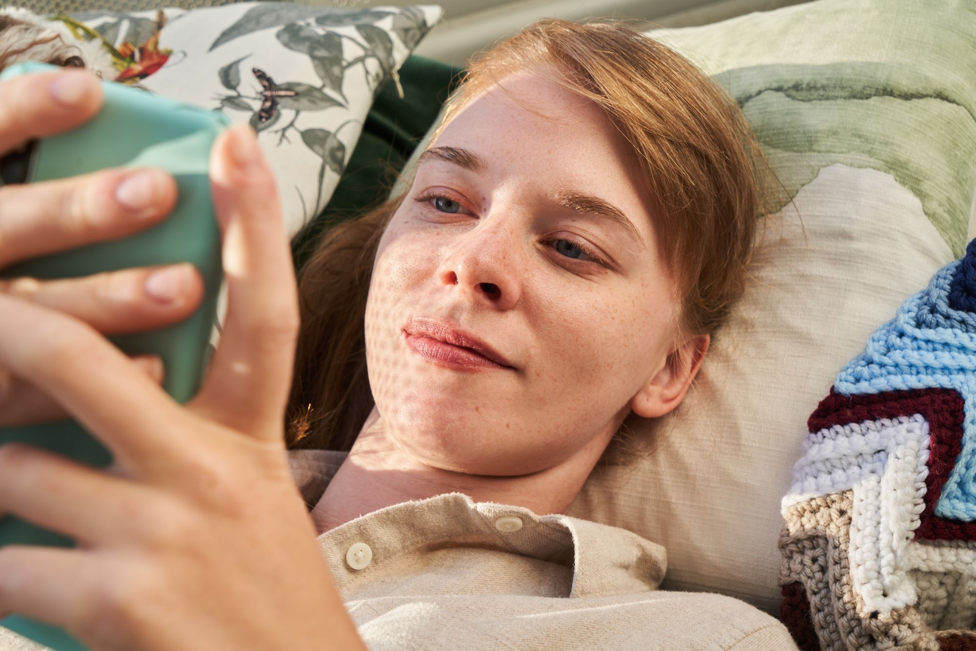 Young woman resting on a pillow looking at her smartphone
