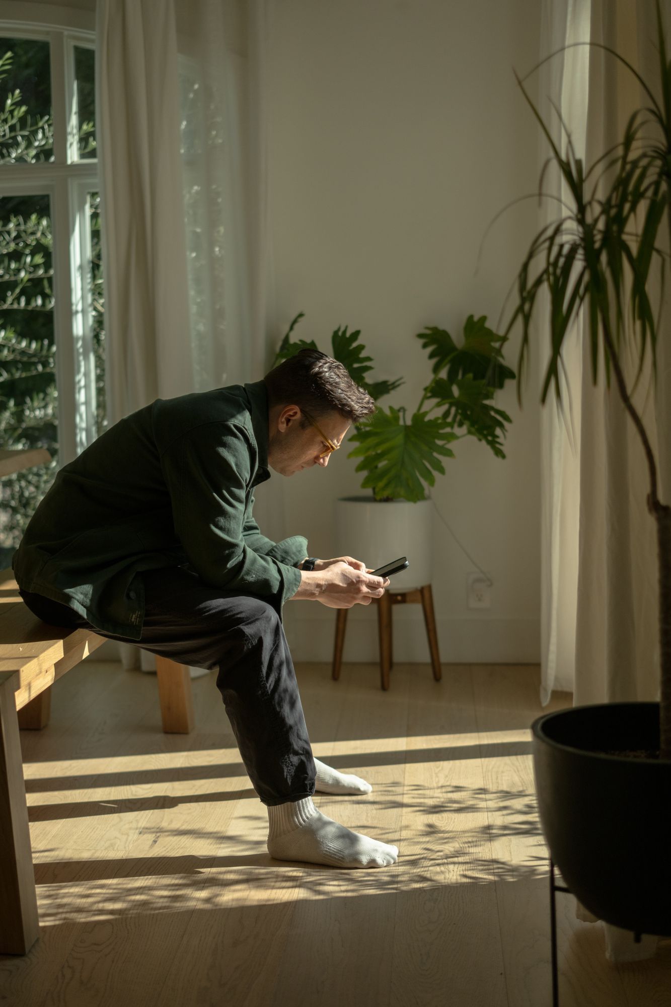 Man wearing glasses looking at his smartphone in a sunlit living room