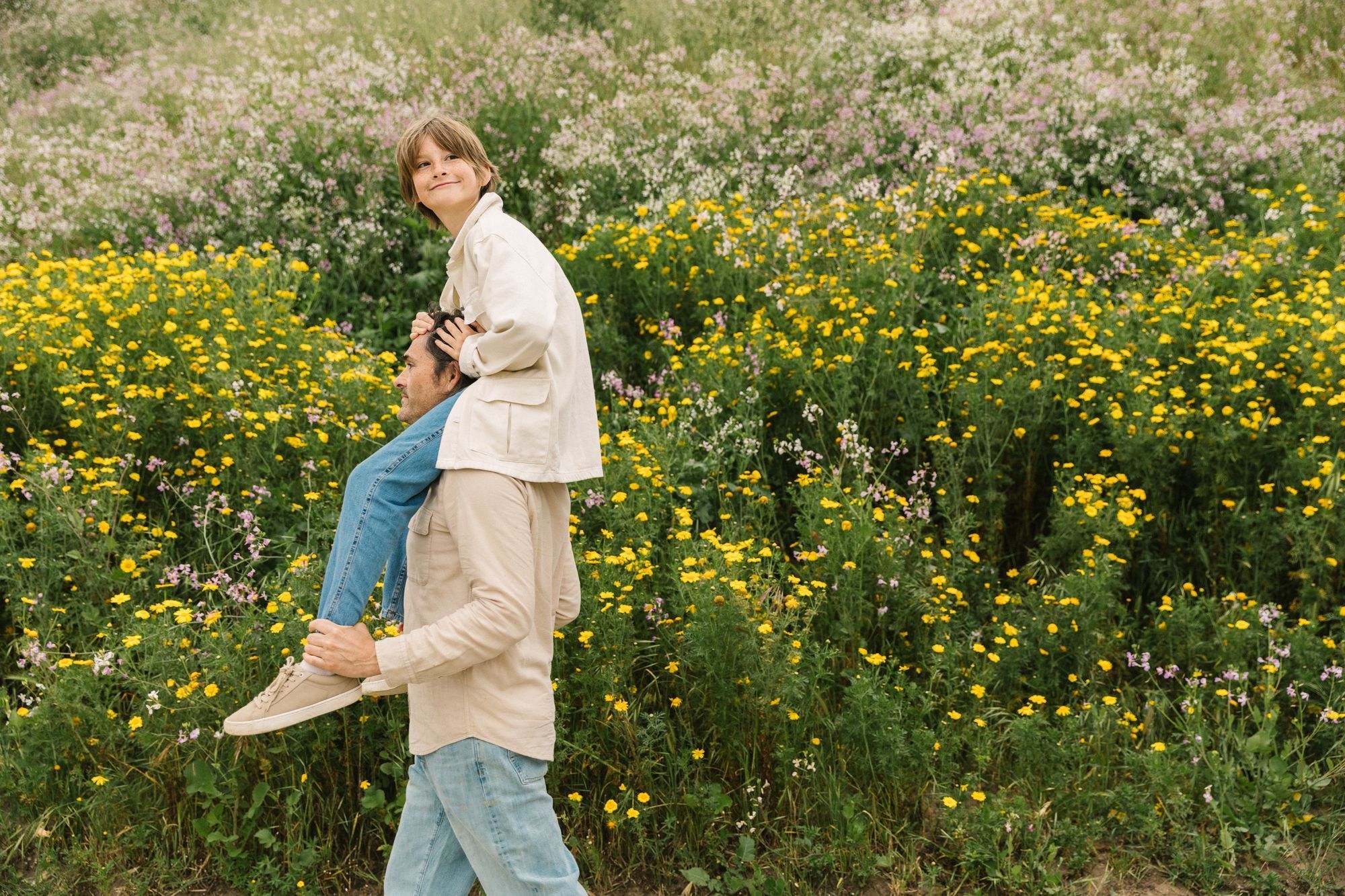 Father carrying his young son on his shoulders outdoors in a field of yellow flowers