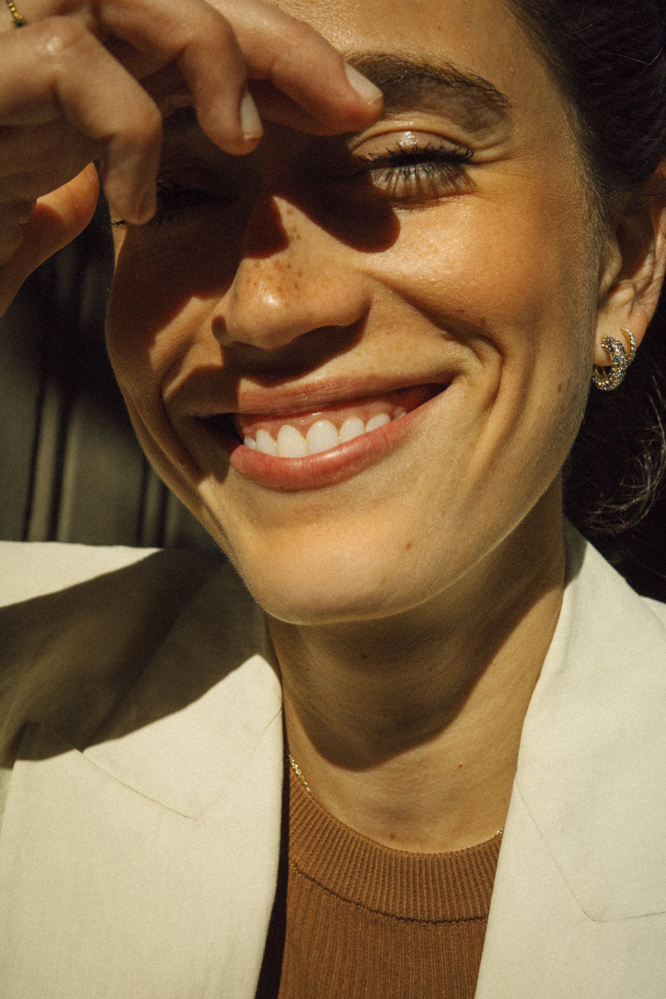 Smiling woman in a white blazer shielding her eyes from sunlight