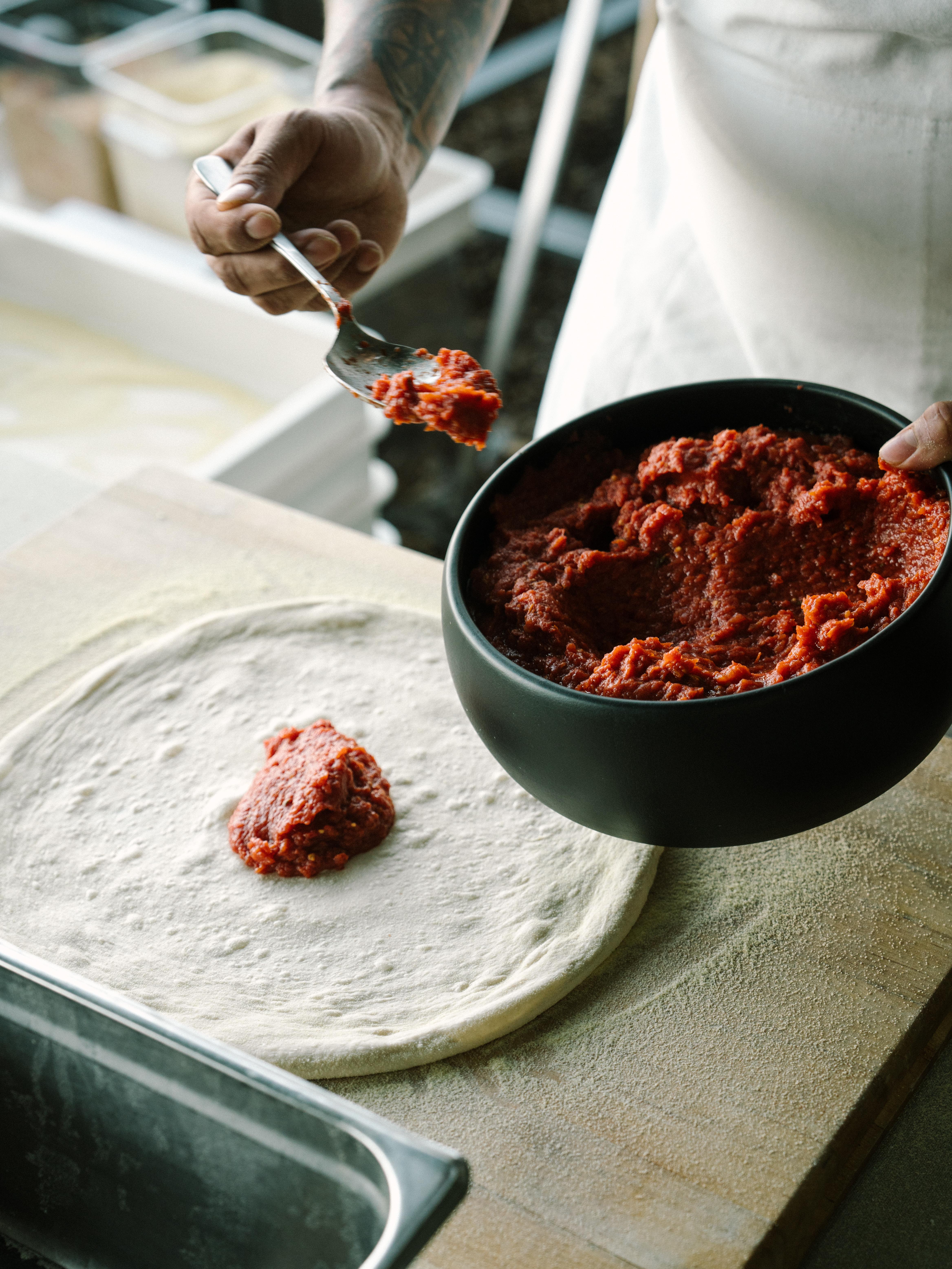 Chef spreading sauce on pizza dough.