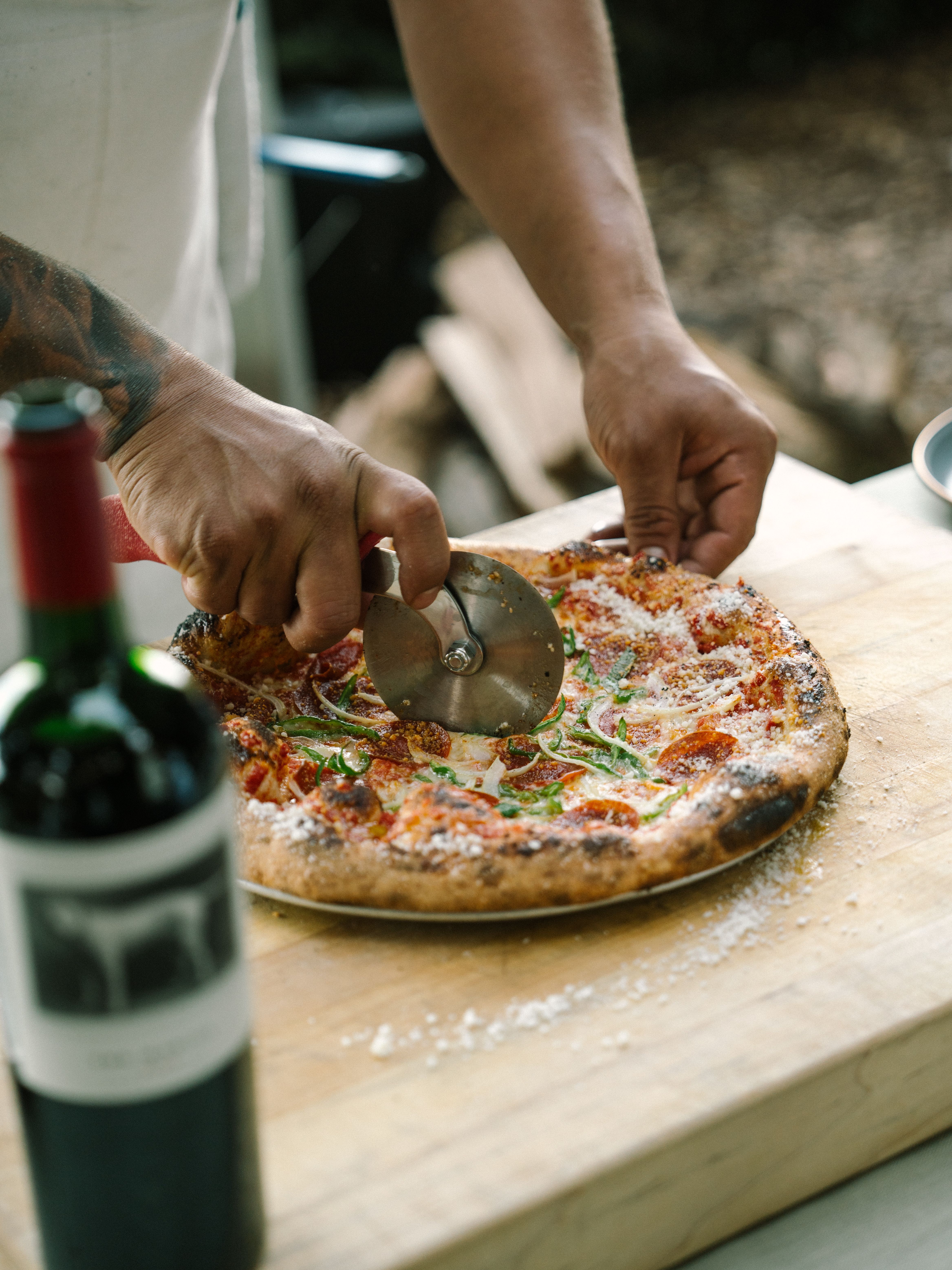 Chef slicing hot pizza next to a bottle of the mascot.